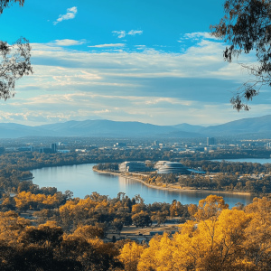 A panoramic view of Canberra with Lake Burley Griffin and mountains in the background, framed by trees with golden leaves.