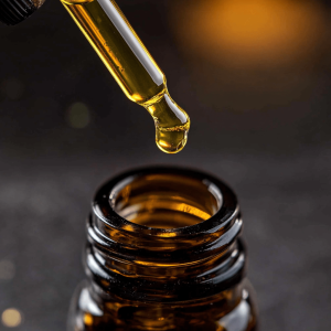 Close-up of a dropper dispensing CBD oil into a glass amber bottle, set against a dark background.