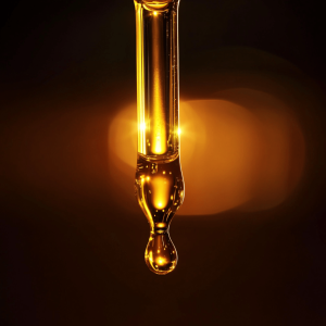 Close-up of a dropper releasing CBD oil with light shining in the background.