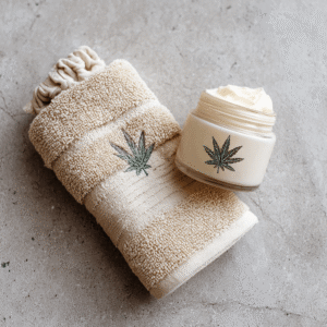 Glass jar of hemp moisturising cream, placed on a beige towel embroidered with a hemp leaf.